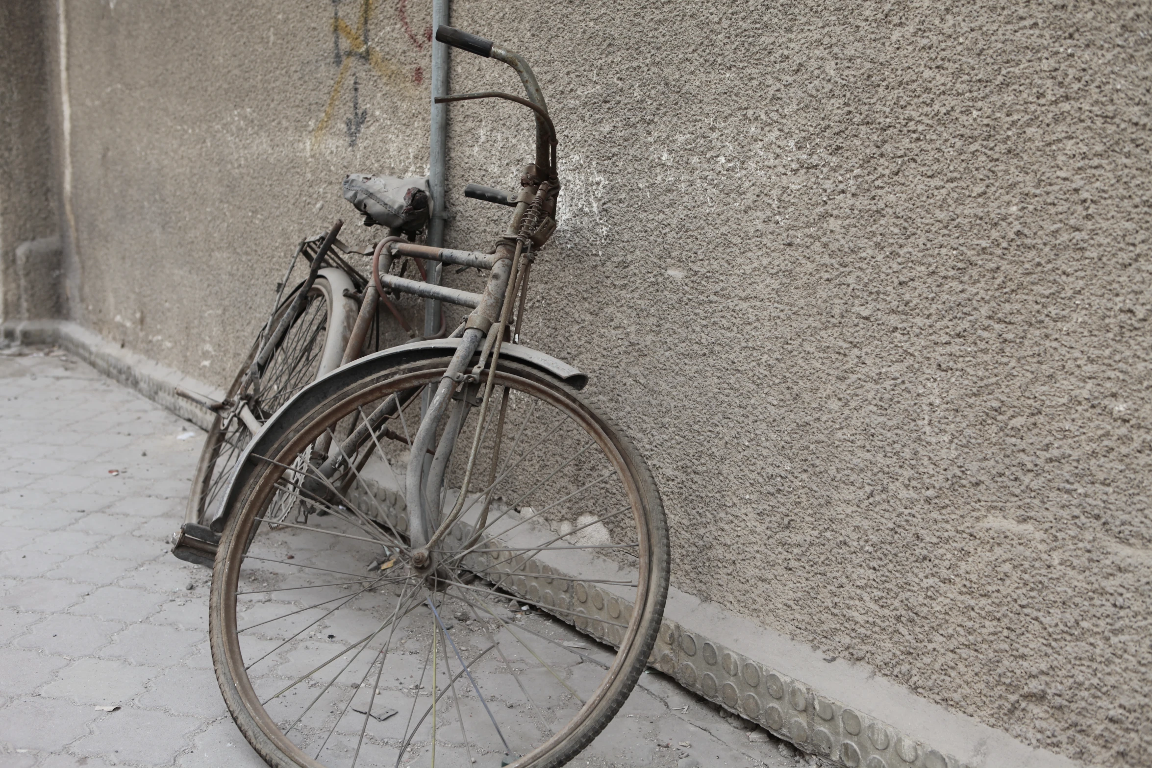 a rusty bicycle leans against a stucco - colored wall