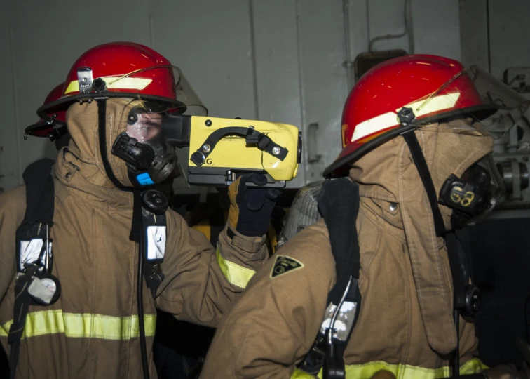 two firefighters in orange uniforms wearing red hard hats and gas masks