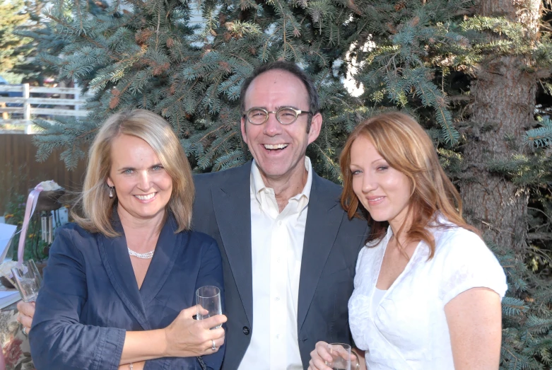 two ladies and a man pose for a picture while holding champagne glasses