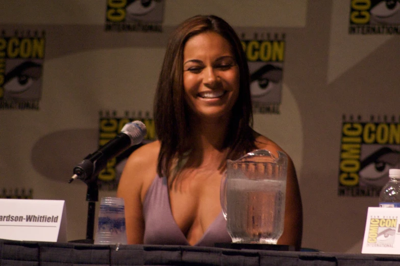 a woman sitting at a table next to a microphone and bottle