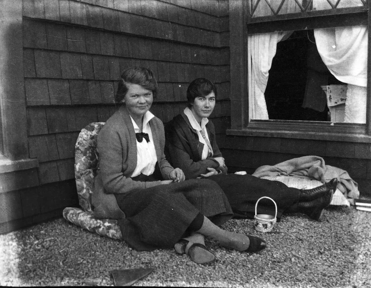 two people sitting on the ground in front of a house