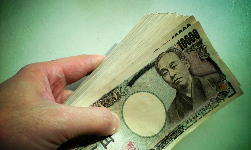 man is holding out folded dollar bill on the table