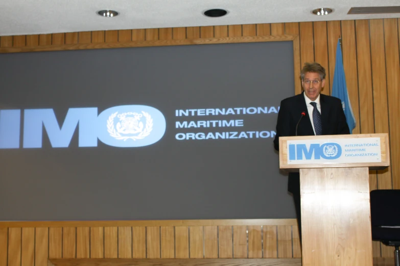 a man standing at a podium in front of the imo sign