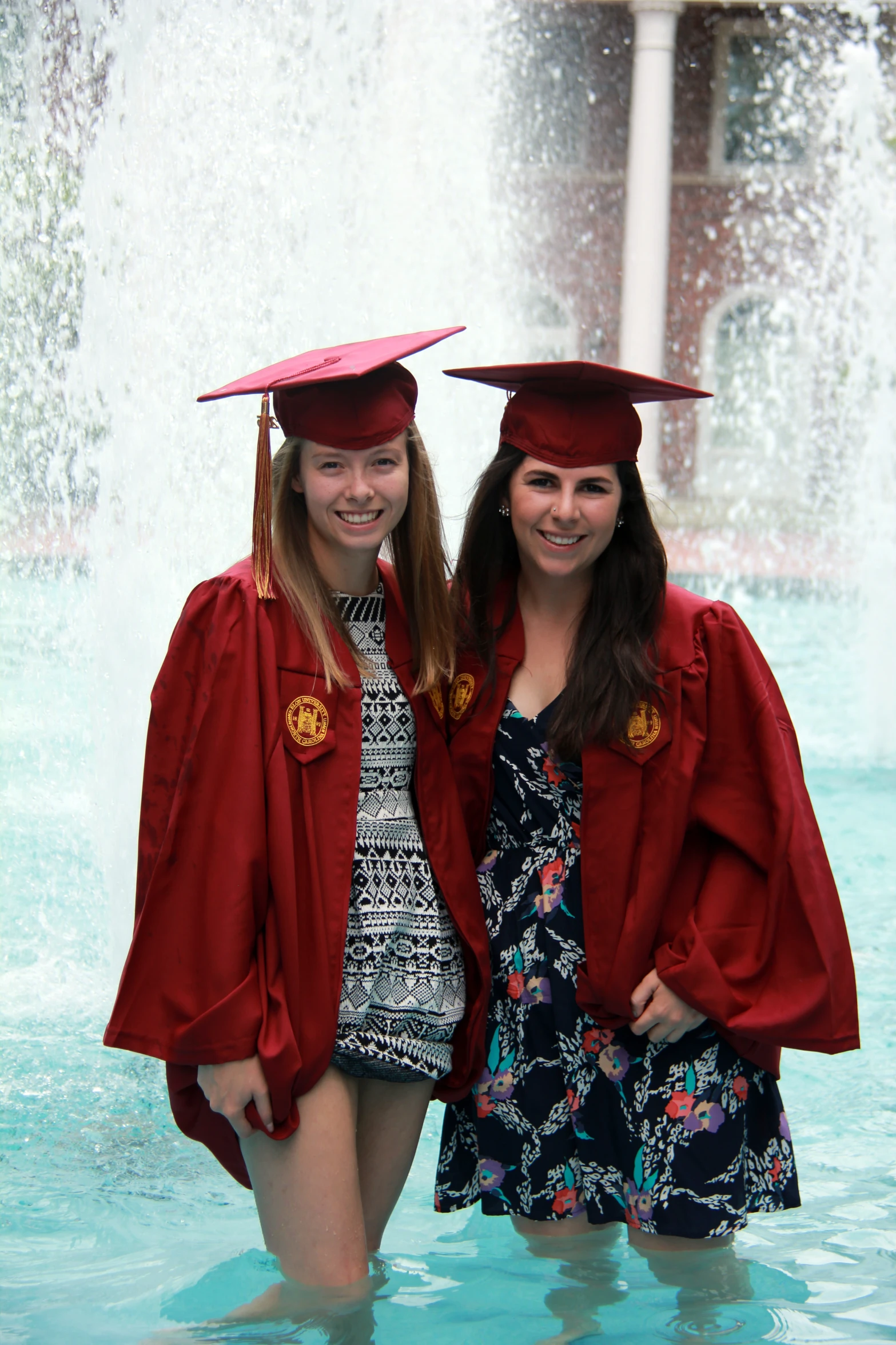 two graduates pose for the camera in front of a fountain