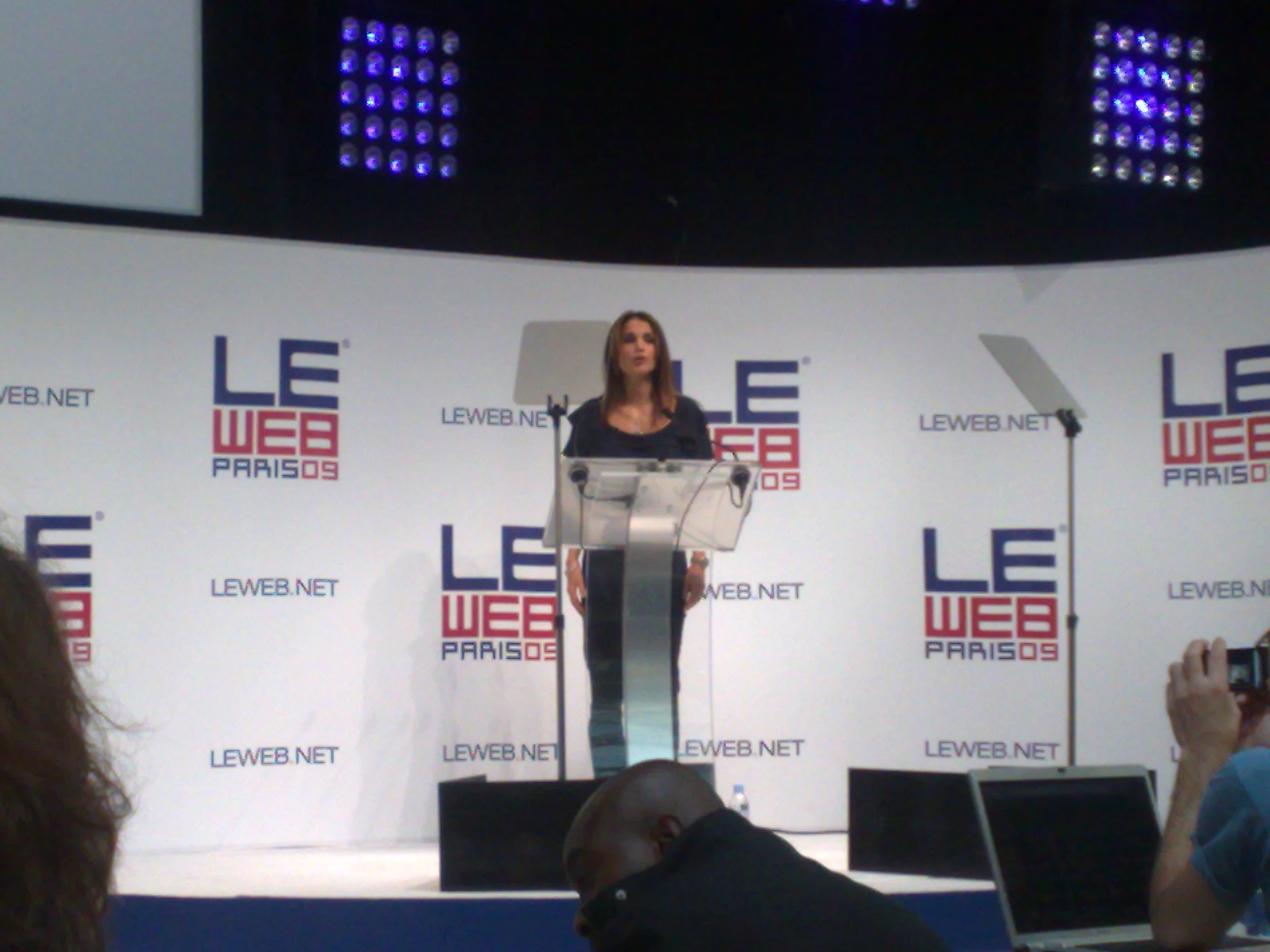 a woman in a black dress stands at a podium as an audience is watching her on the sidelines