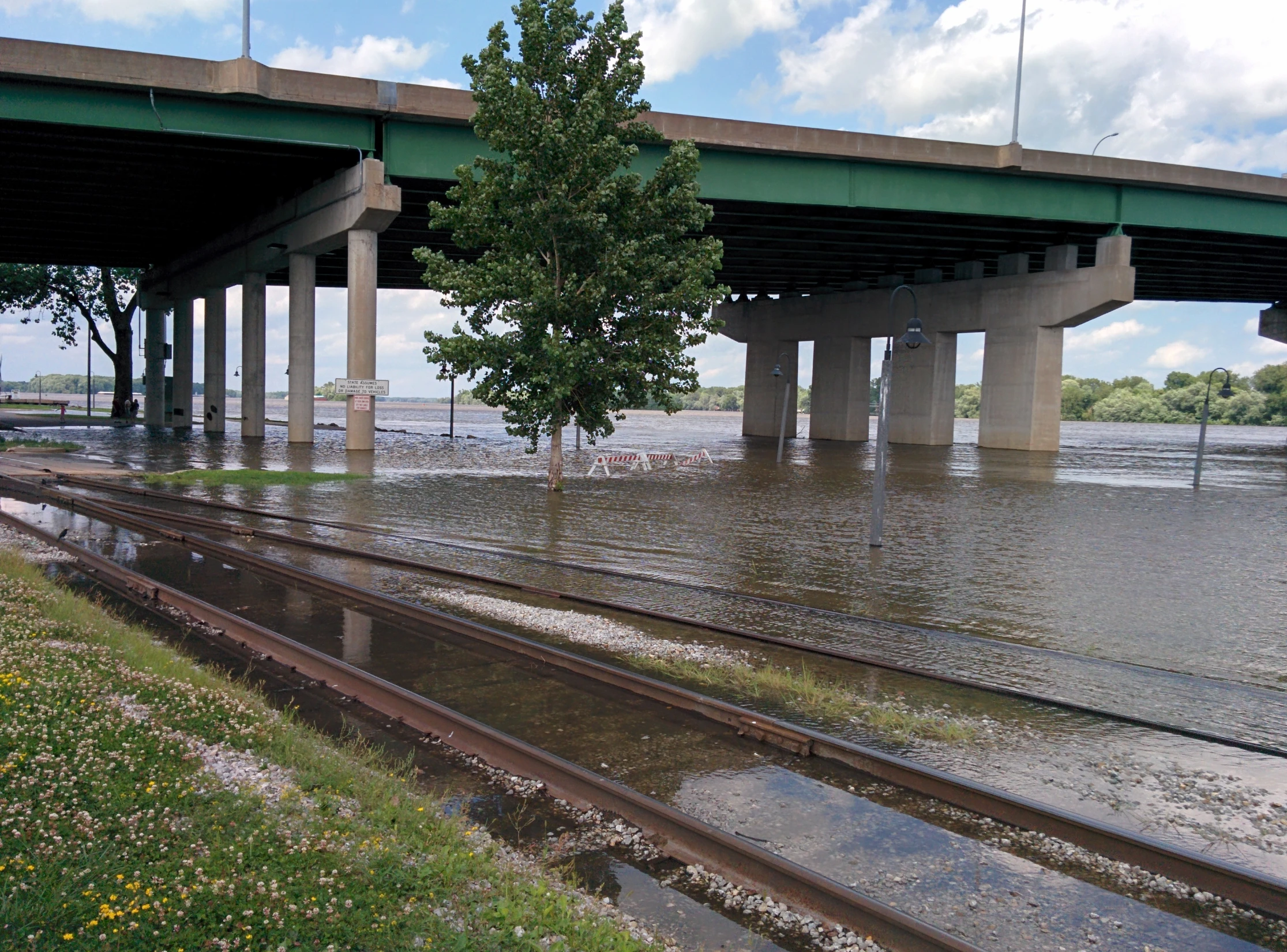 flooded road with water flowing under bridge above