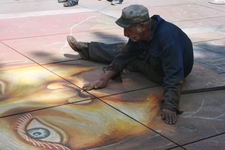 man sitting on the sidewalk drawing a face with colored pencil