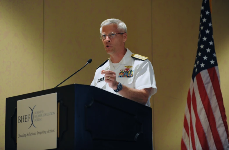 an army man speaking at a podium with the american flag