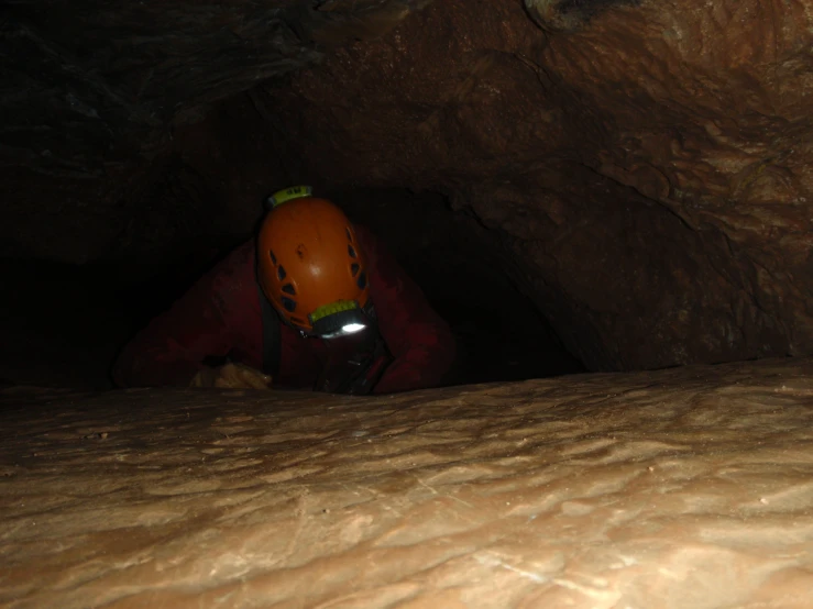 an adult in a red jacket and orange helmet in a cave