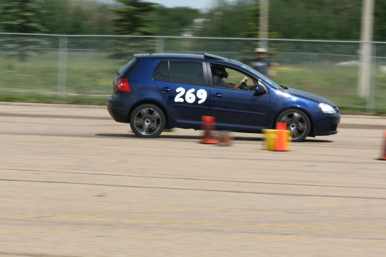 an orange traffic cone and car passing by on a race track