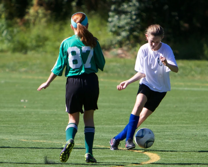 two young women kicking a soccer ball around a field