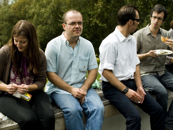 a group of people sitting on a wall next to each other eating food