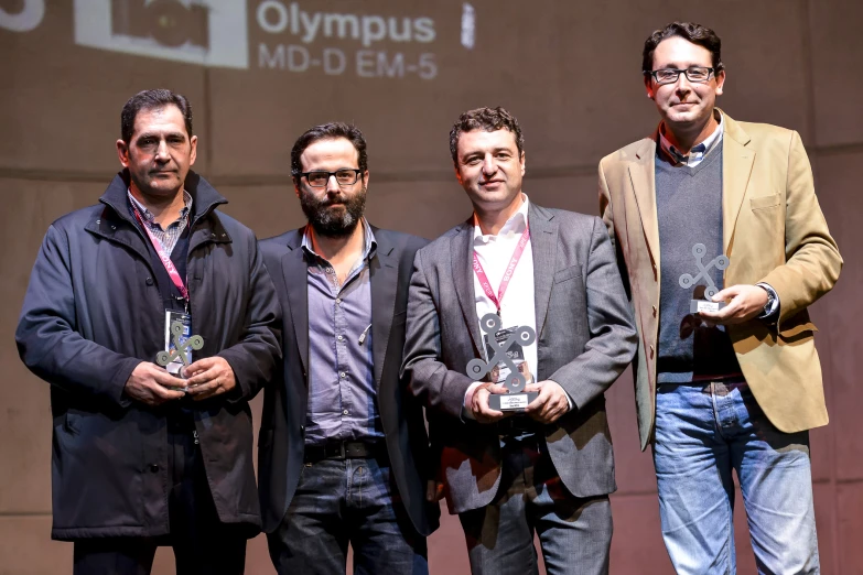 three men holding their trophies while standing on a stage