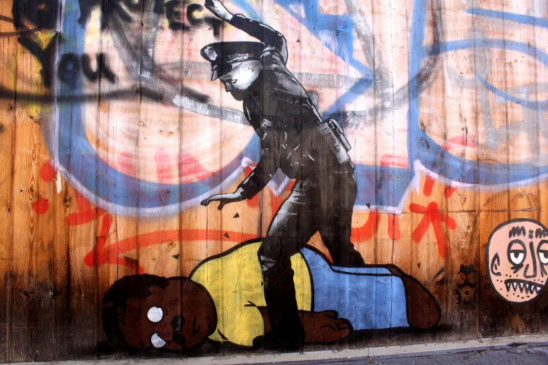 a wooden fence with graffiti and a man with a blue jacket walking towards a stuffed animal