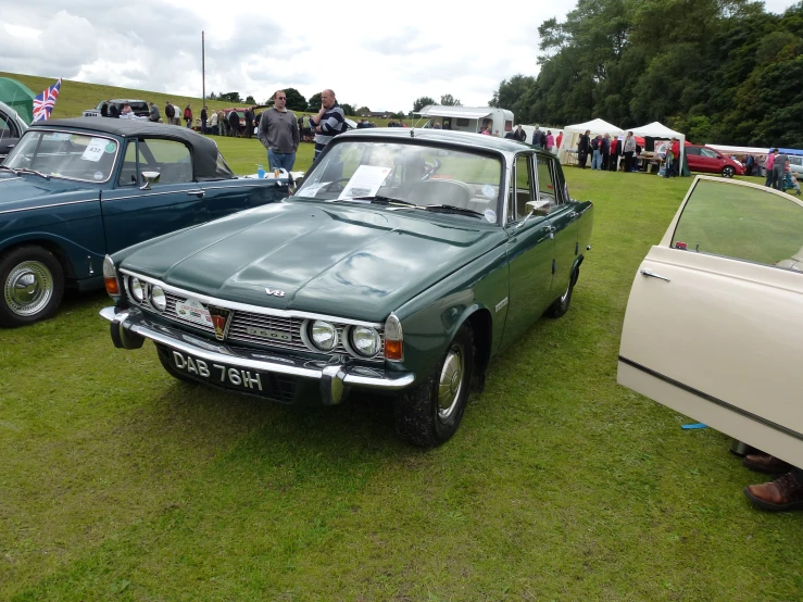 old cars parked on the grass in front of people