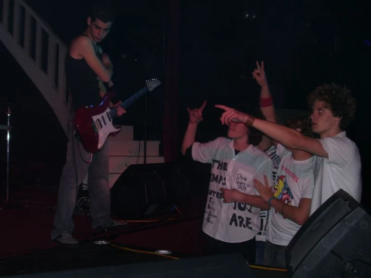 two guys playing guitar at an event while another watches