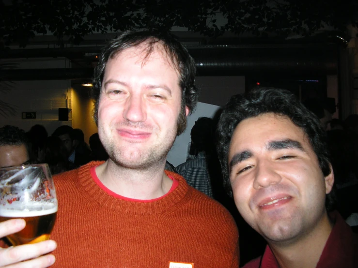 a man smiles as he poses with another person holding a glass