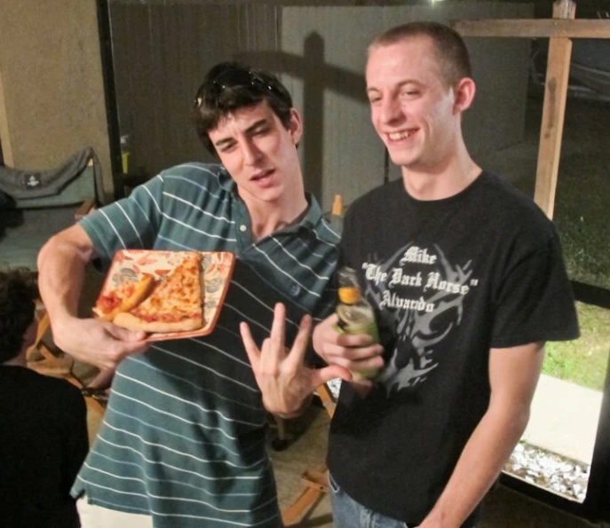 a man holding an open glass with his finger next to another man eating pizza