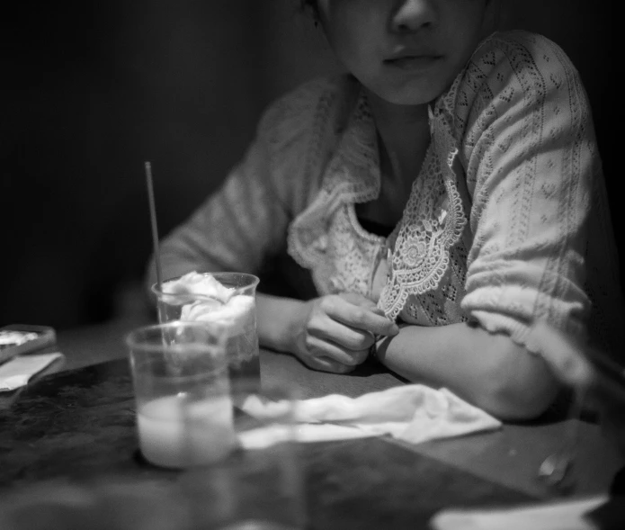the young woman sits at a table with a drink in her hand