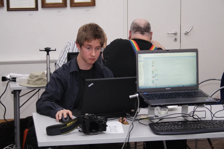 two people sitting at a desk in front of two laptops