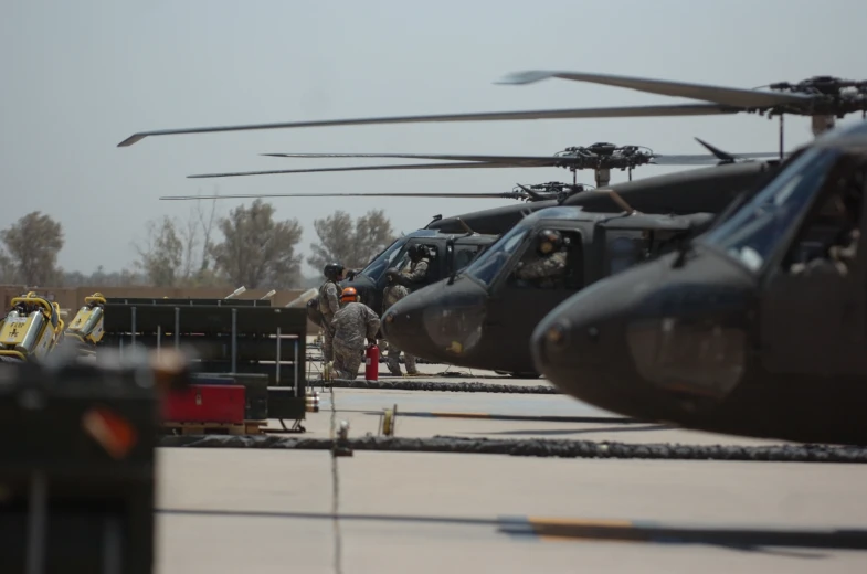 many people in uniform stand near military helicopters