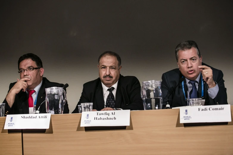 three men sitting at a table in front of microphones