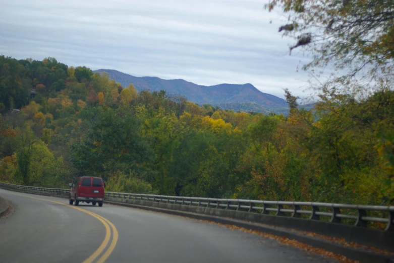 a vehicle drives on the road next to a wooded landscape