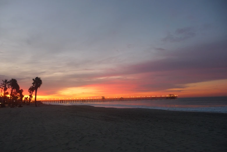 a beach view with palm trees and the sun setting over the water