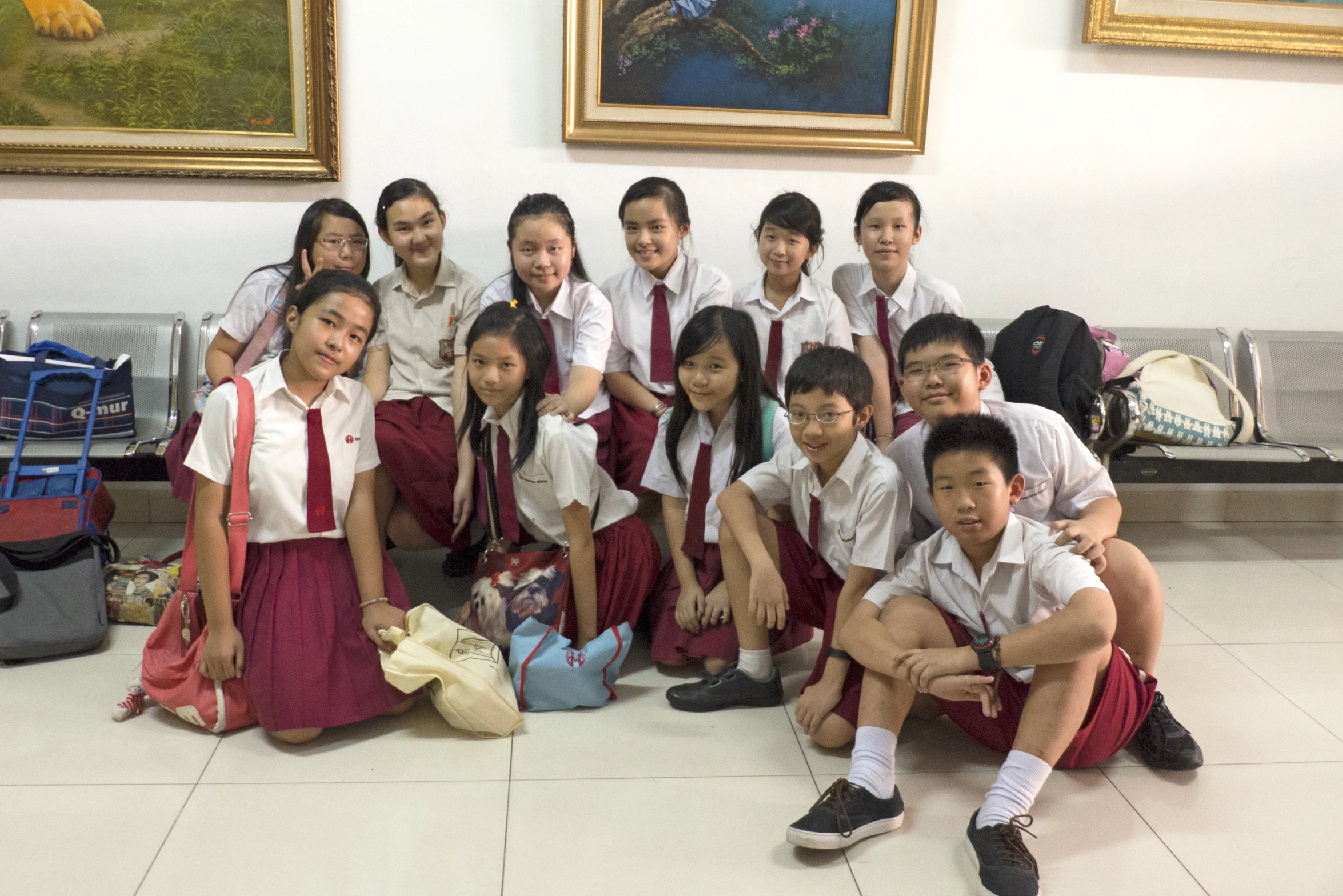 a group of school students sit on the ground in front of a painting