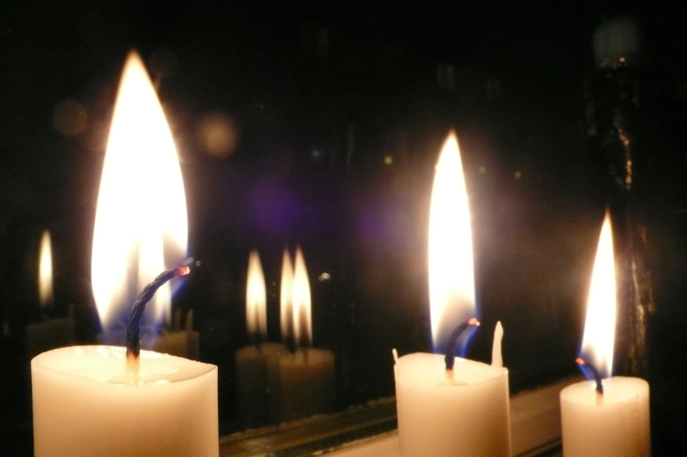 three lit candles with some of the lights on