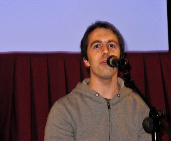 man talking into a microphone with the projection screen behind him