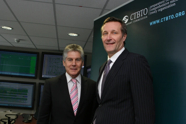 two men posing next to each other in front of monitors