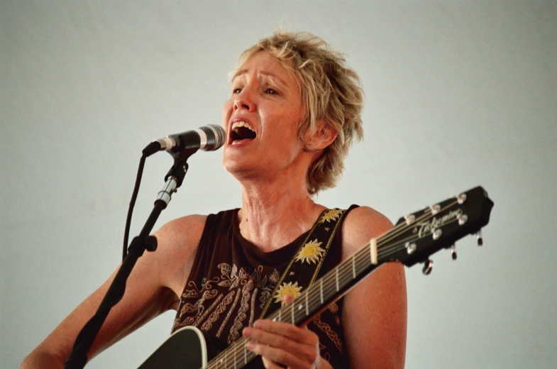 a woman singing into a microphone and holding an acoustic guitar