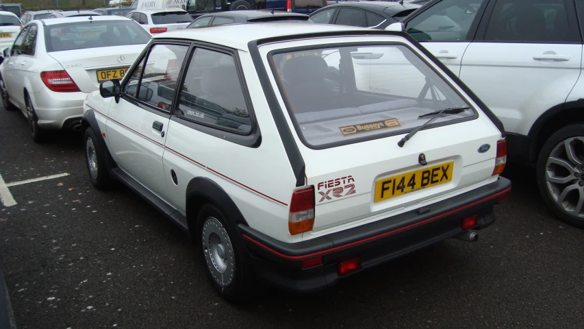 a small white car parked in a lot near other cars