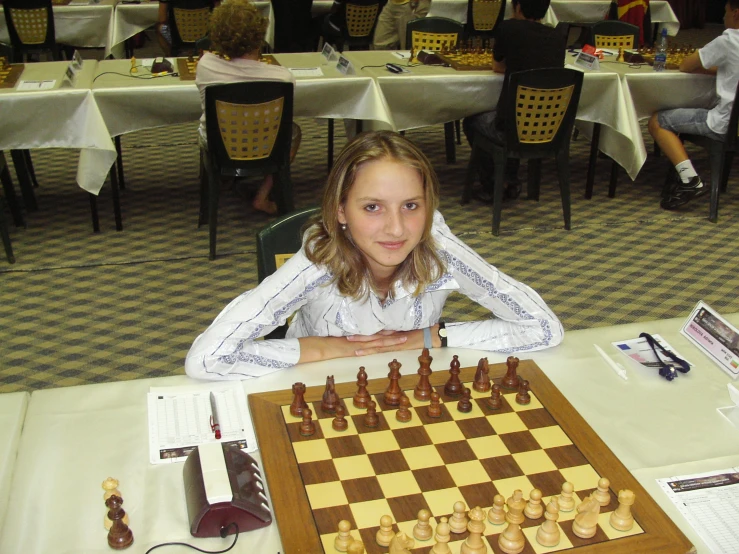 a girl is sitting at a table with chess set