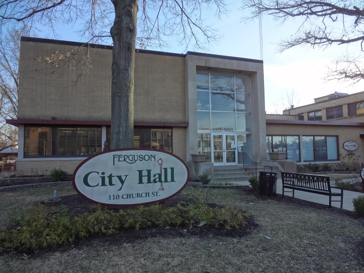 a brick city hall is in front of a large tree