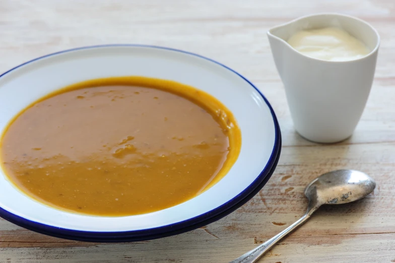 a bowl of soup and a cup of cream on a wooden surface