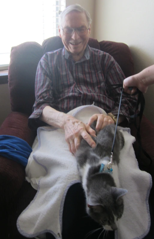 an elderly man holding on to a cat on top of a chair