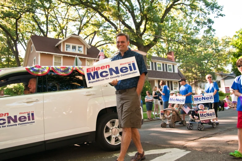 a man is holding a campaign sign with a parade in the background