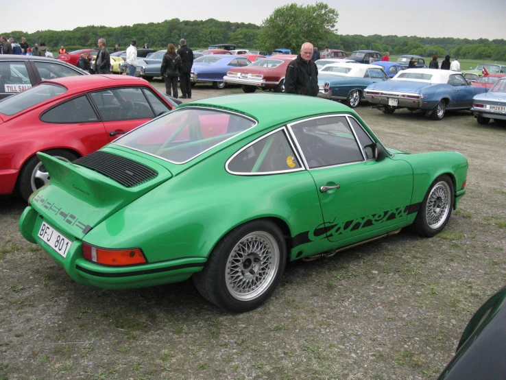 a group of men standing around two green porsches