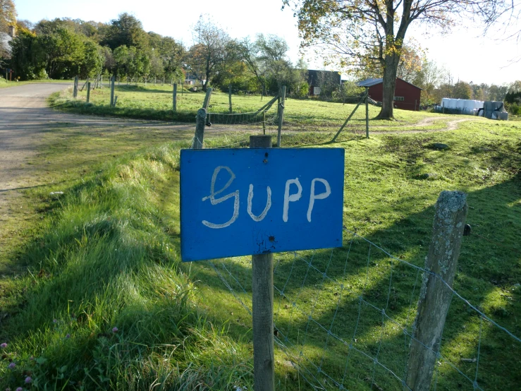 a blue sign is near the fence to a field