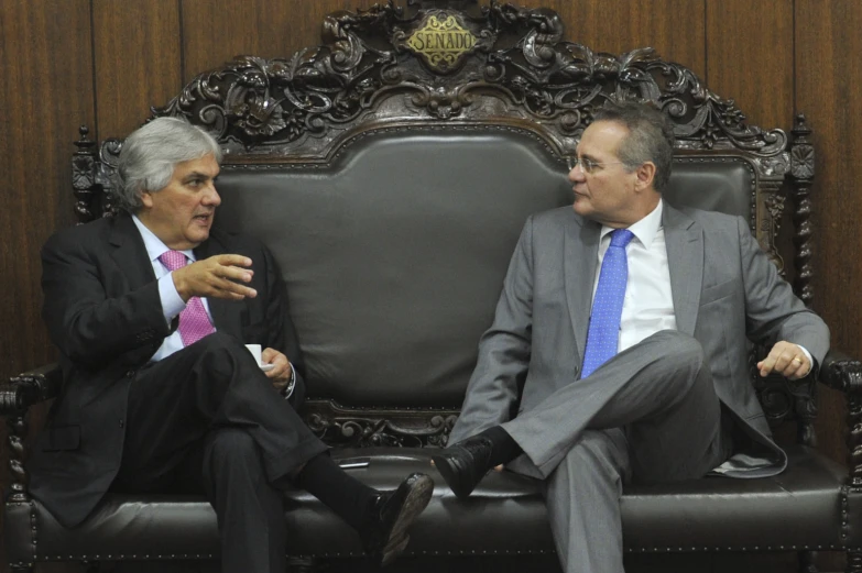 two men in suits sitting on a bench talking