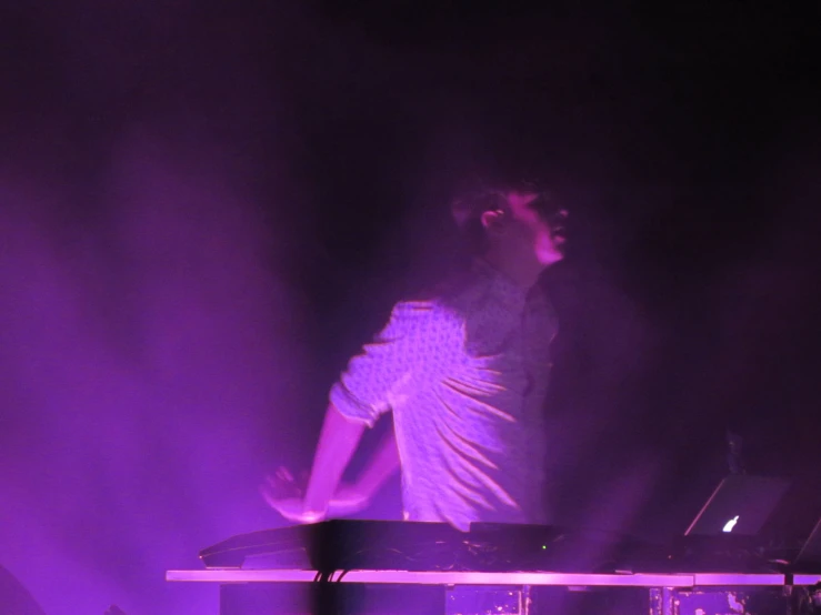 man in white shirt standing at stage with purple lighting