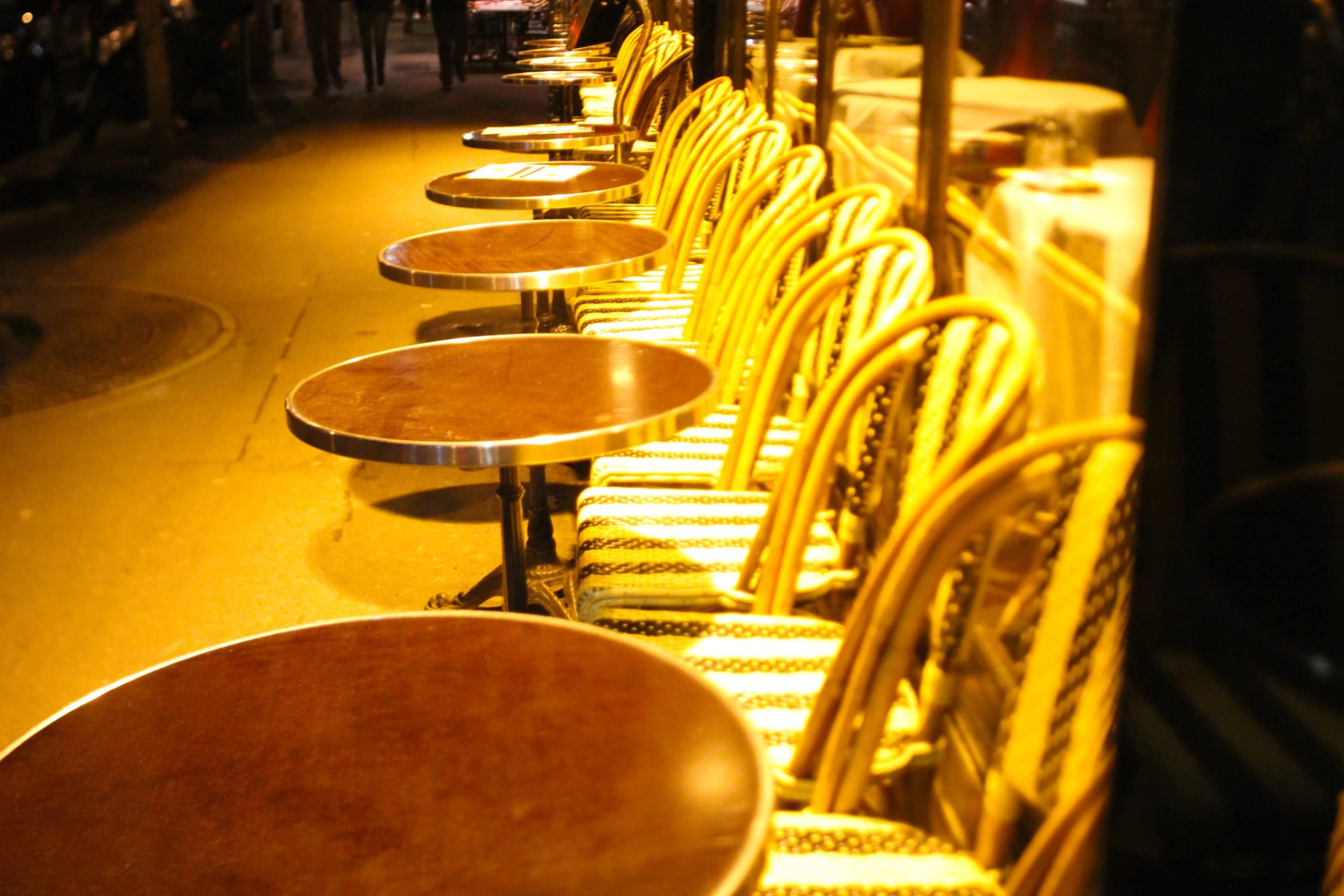 empty tables line up on a sidewalk in the dark