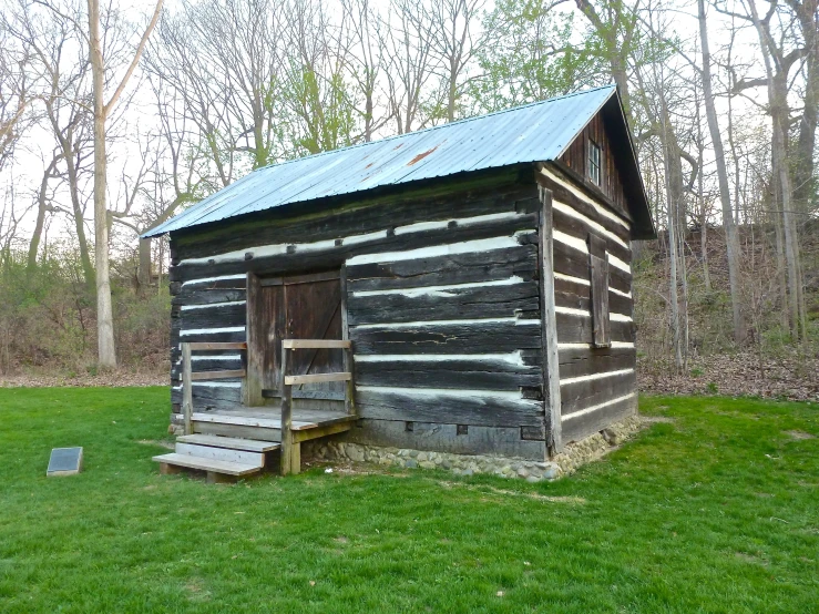 a small log cabin in a field with grass and trees