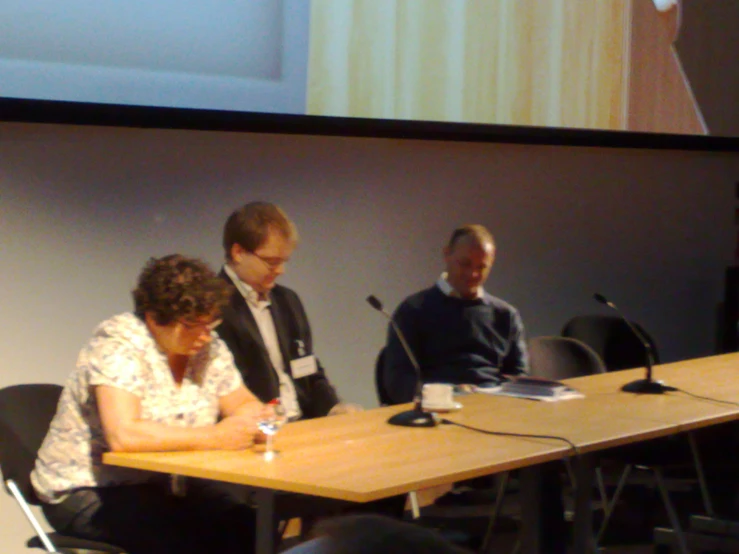 three people sit at a table, speaking into microphones