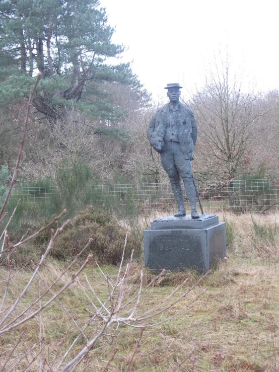 statue of a man holding his hat standing in the grass