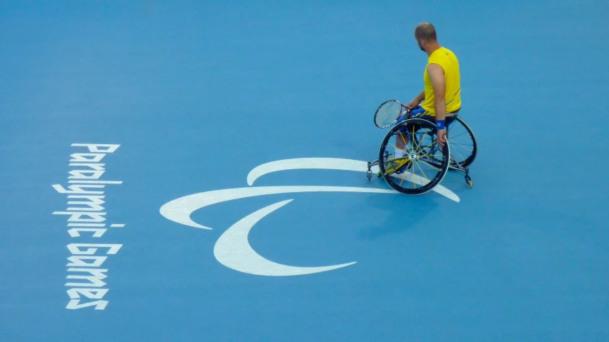 a man in yellow shirt and blue shorts holding tennis racquets