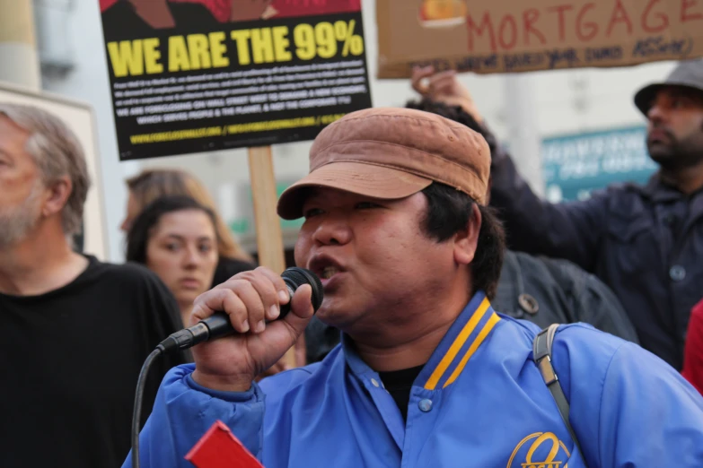 a man speaking into a microphone next to a group of people holding signs