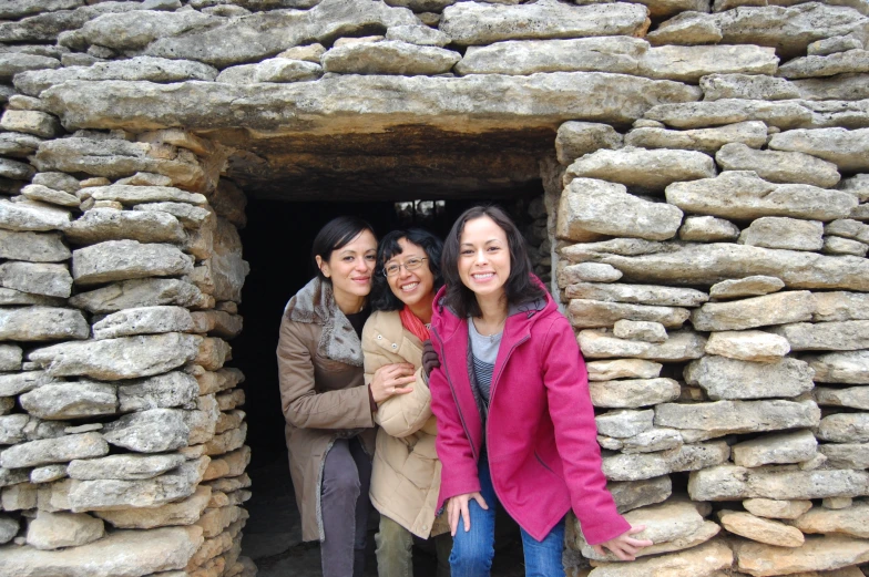 three women standing next to each other in front of a stone structure